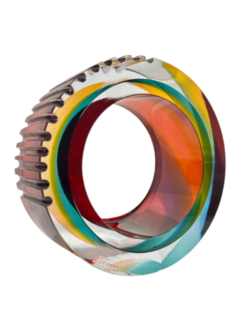 glass cylinder with cog like slices on one side, swirls of orange blue and yellow