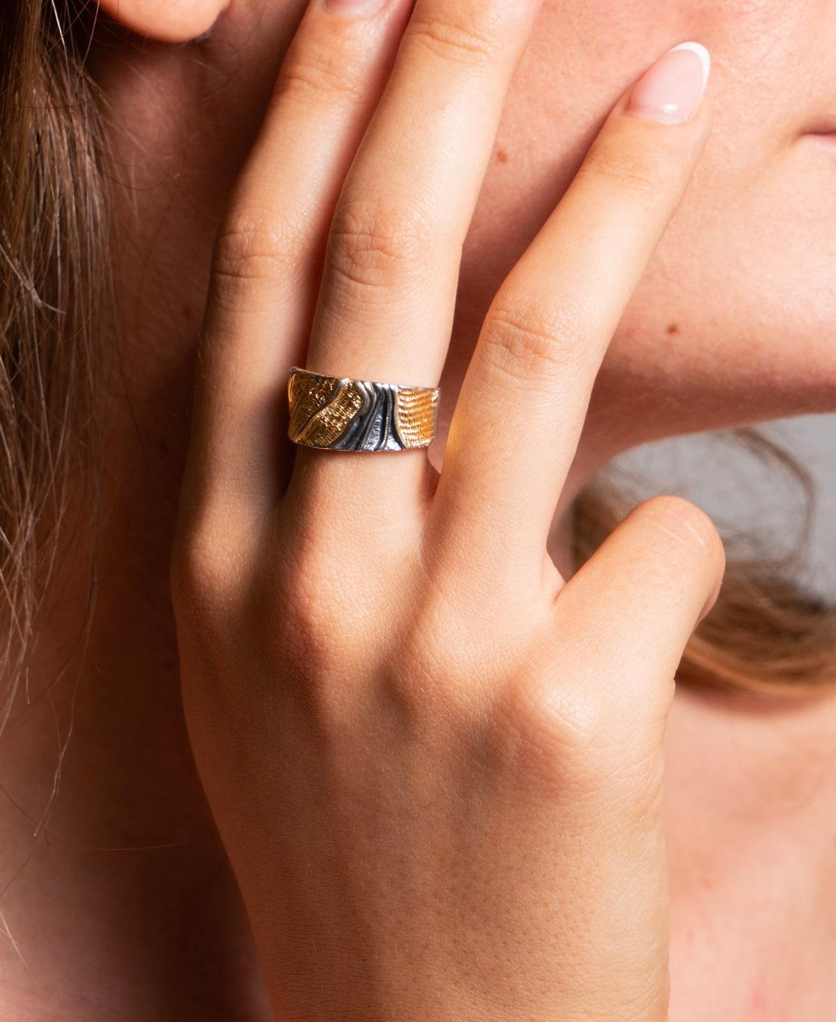 A close-up of a person's hand wearing a textured two-tone ring with gold and silver bands.