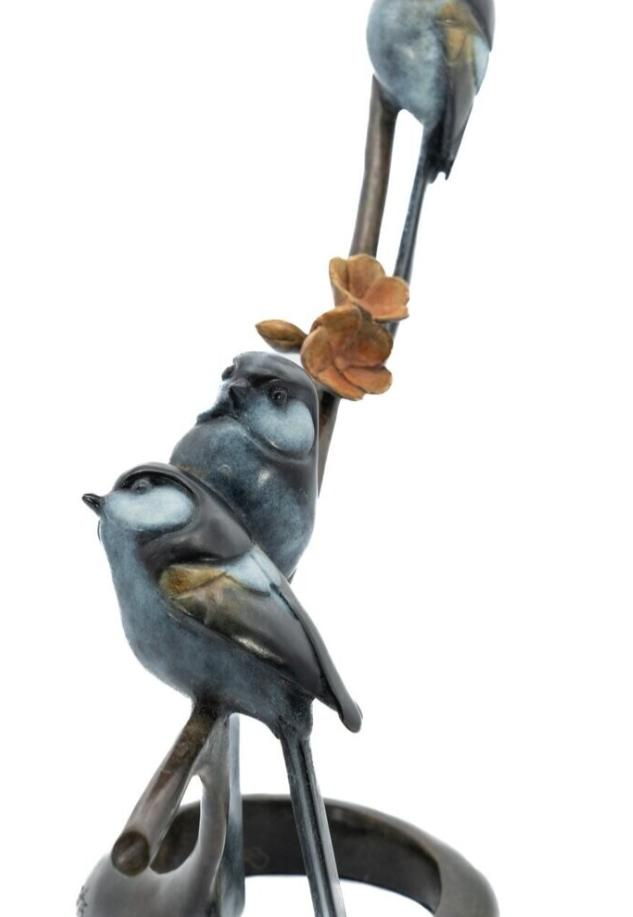 Statue of three birds perched on a branch with leaves against a white background