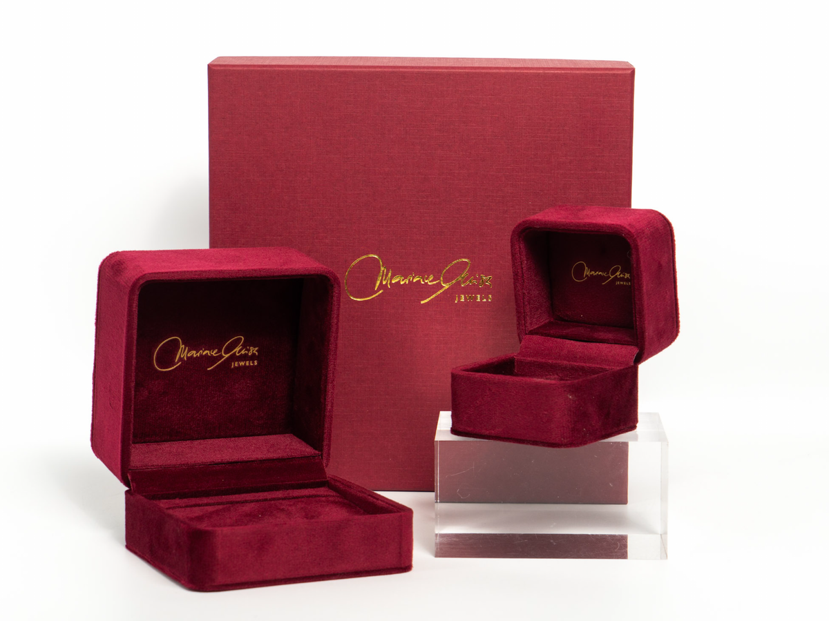 Three burgundy velvet jewelry boxes from Omnia Gold, including one large closed presentation box, one open box, and one smaller open box displayed on a clear acrylic riser, against a white background.