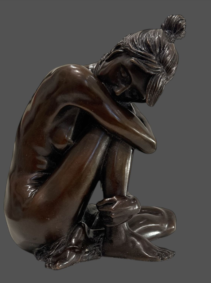 Bronze sculpture of a person sitting with hands over head on a gray background