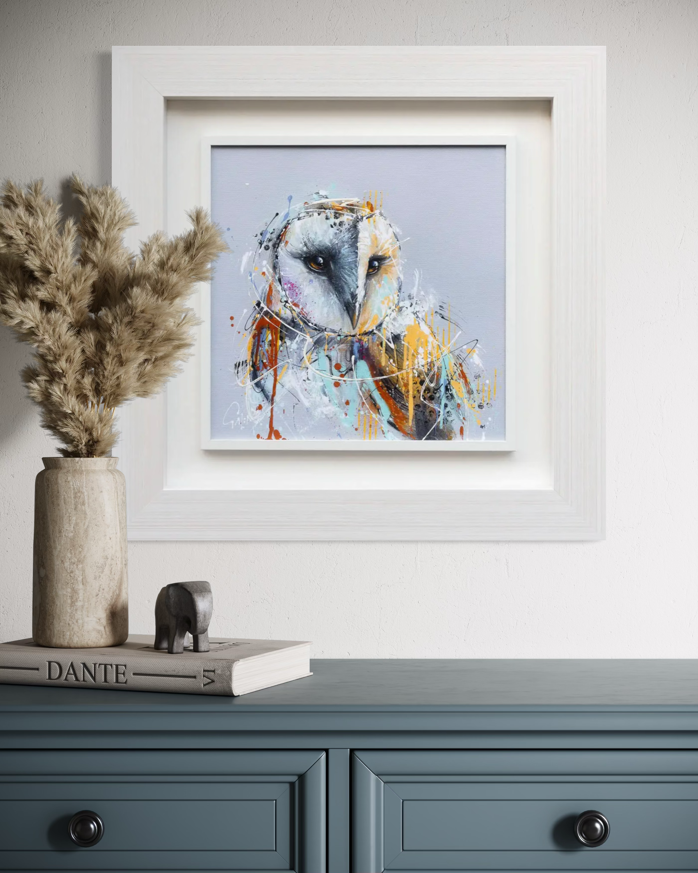 Framed abstract art of a owl's face on a wall above a blue cabinet.