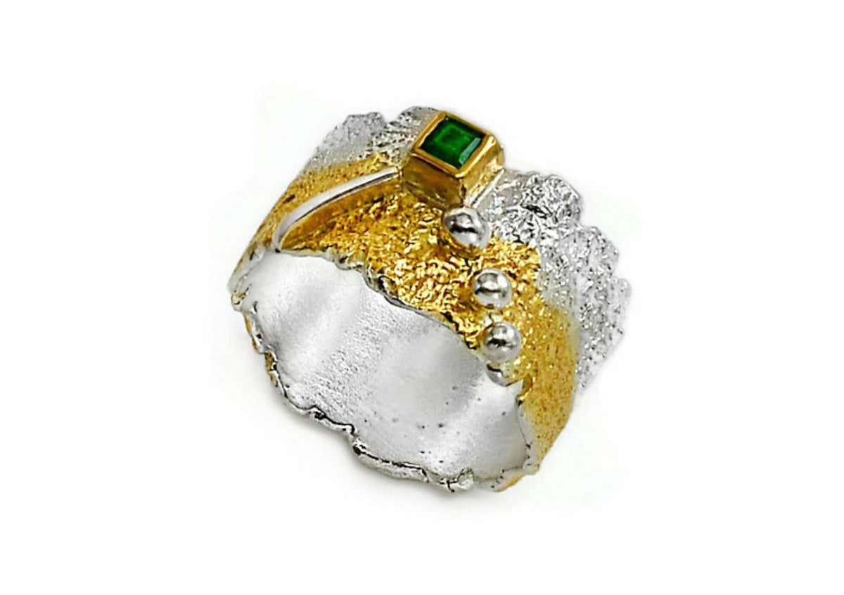 Silver and gold ring with a green gemstone on a white background