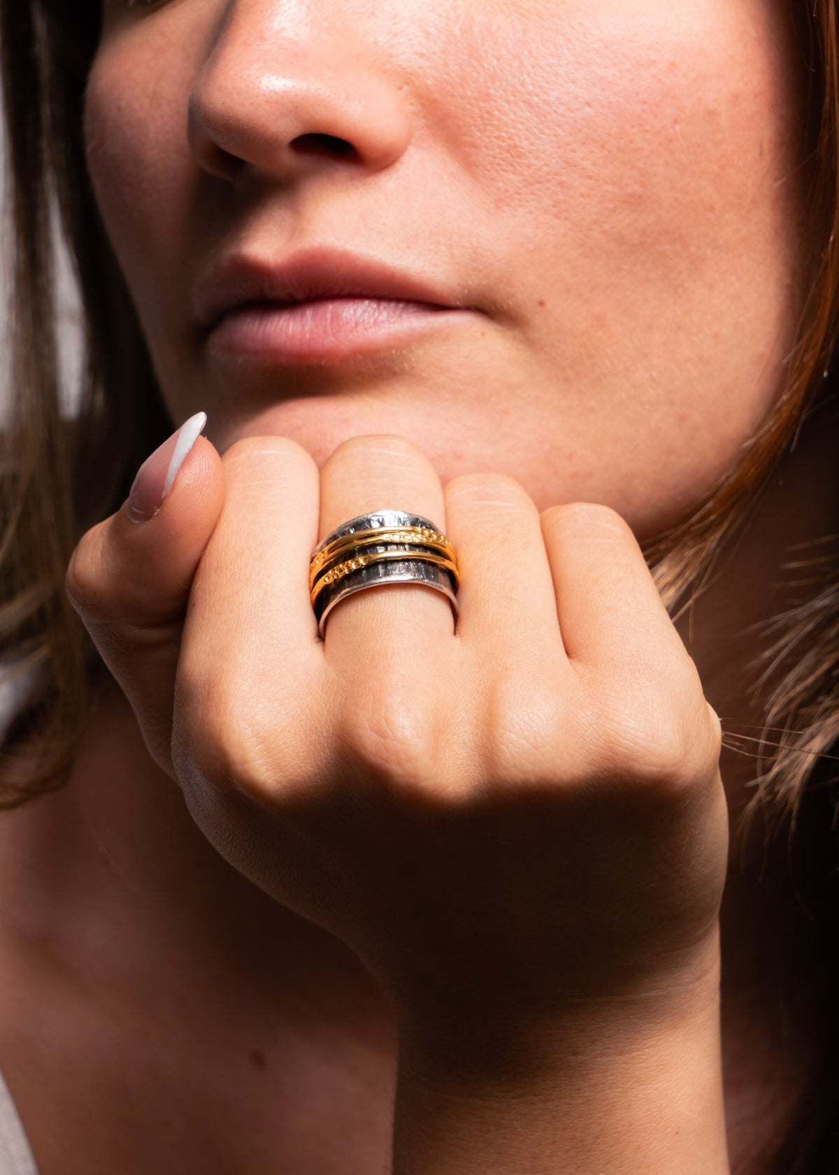 A close-up of a woman's hand resting near her chin, wearing a stack of three metallic rings in gold, silver, and white gold.