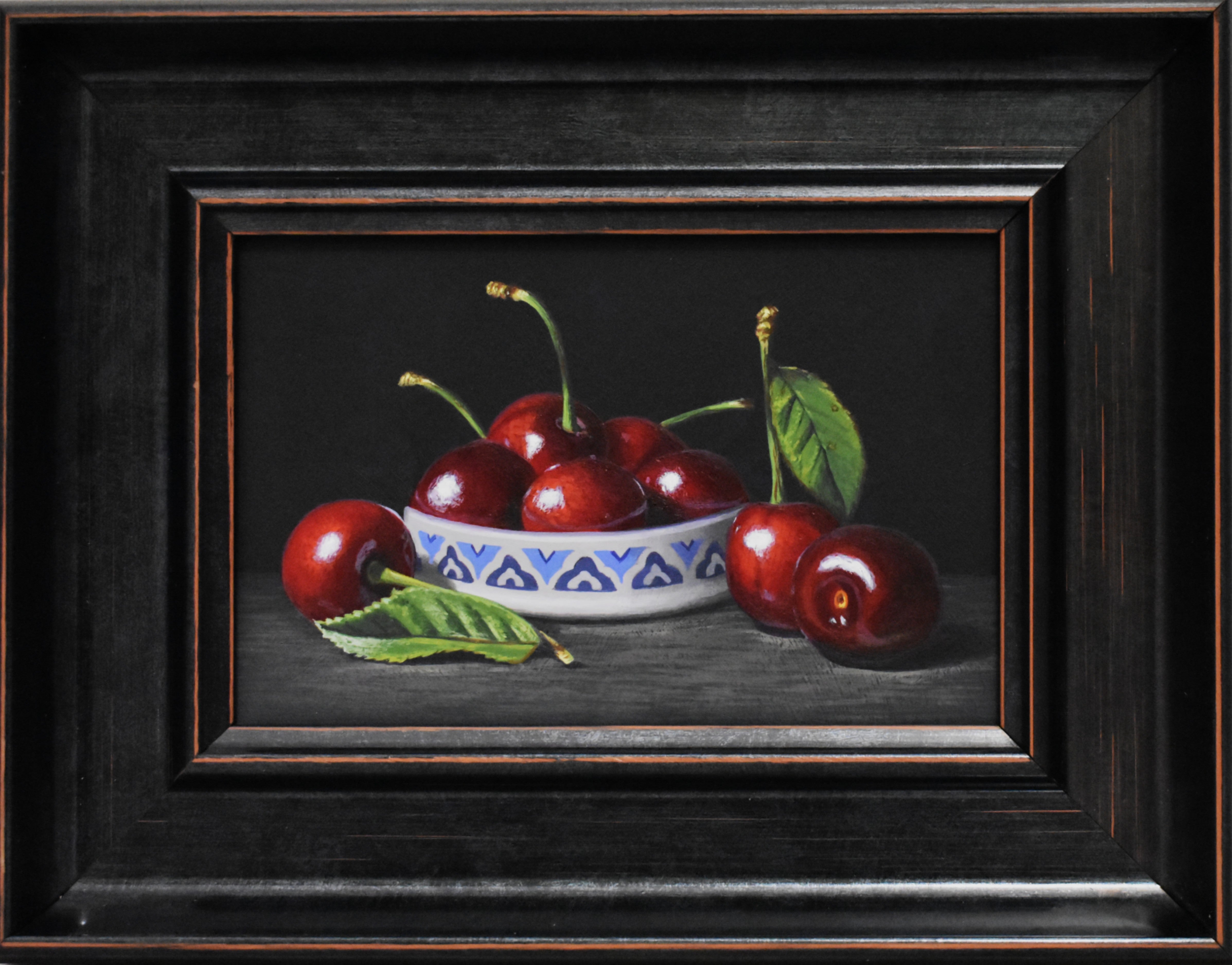 Framed still life of cherries sat in a white and blue ceramic pot