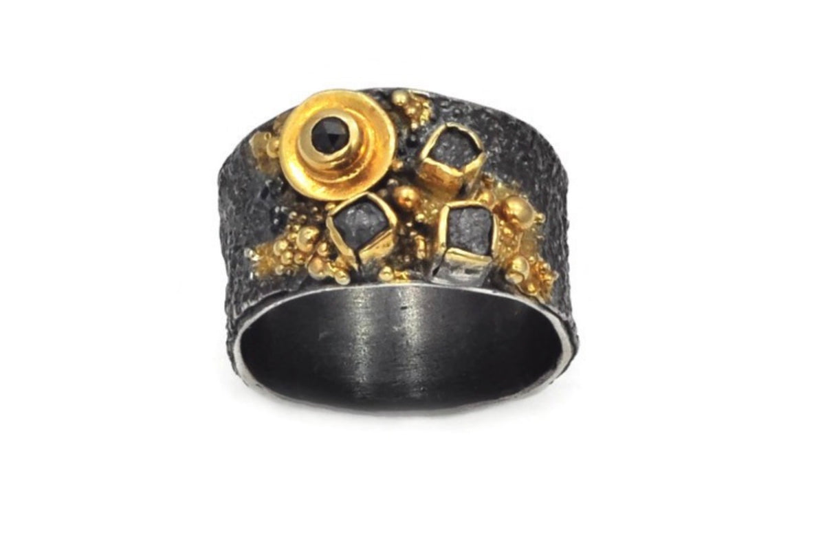 A close up of an oxidised ring with black diamond and rough diamonds with gold vermeil detailing by Eva Stone