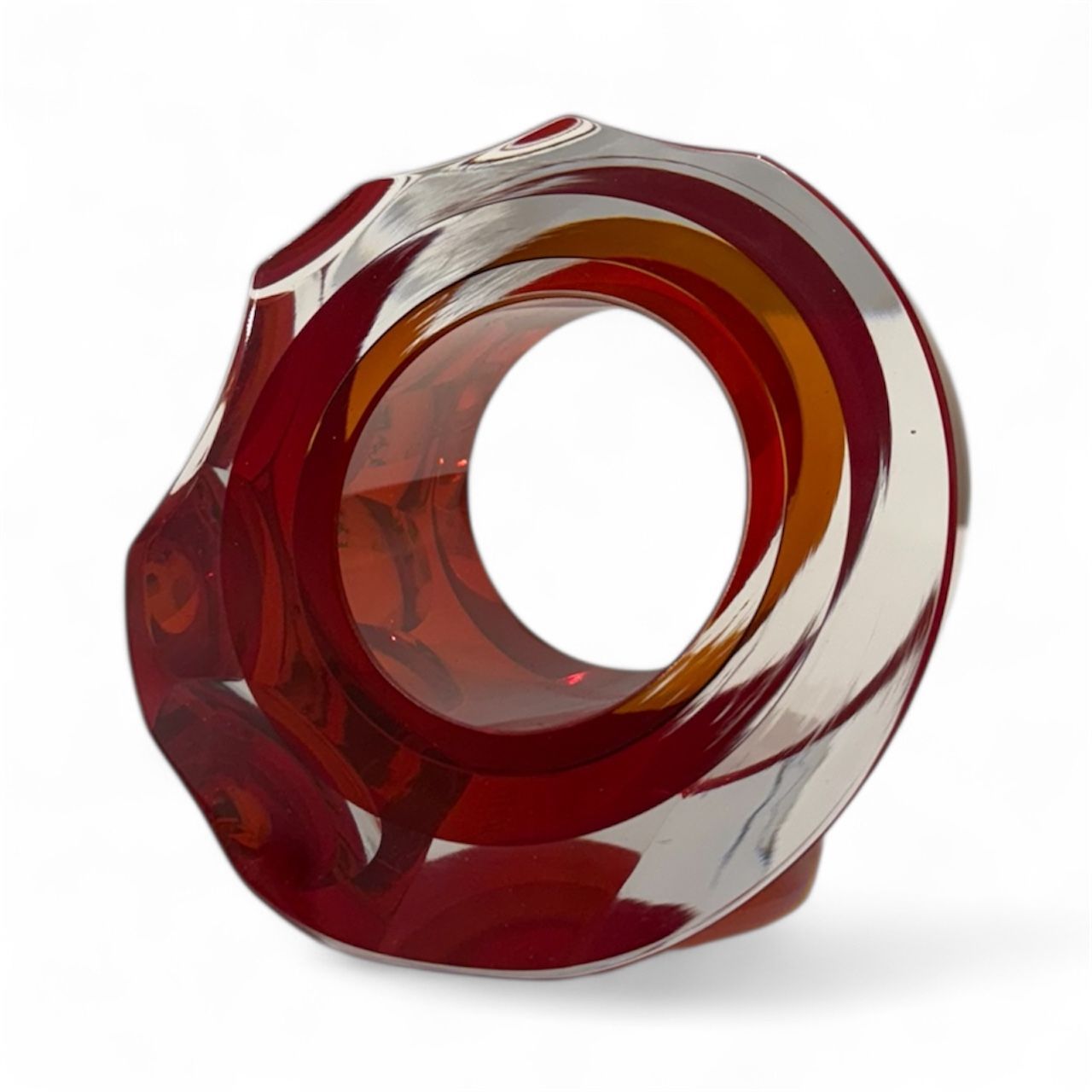 Colorful glass sculpture with red, orange, and clear swirls on a white background