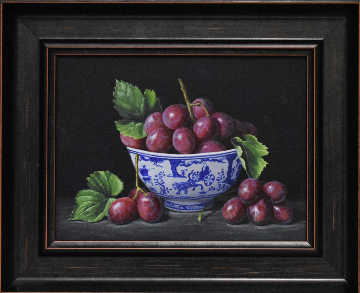 Still life painting of grapes in a blue and white bowl on a dark background