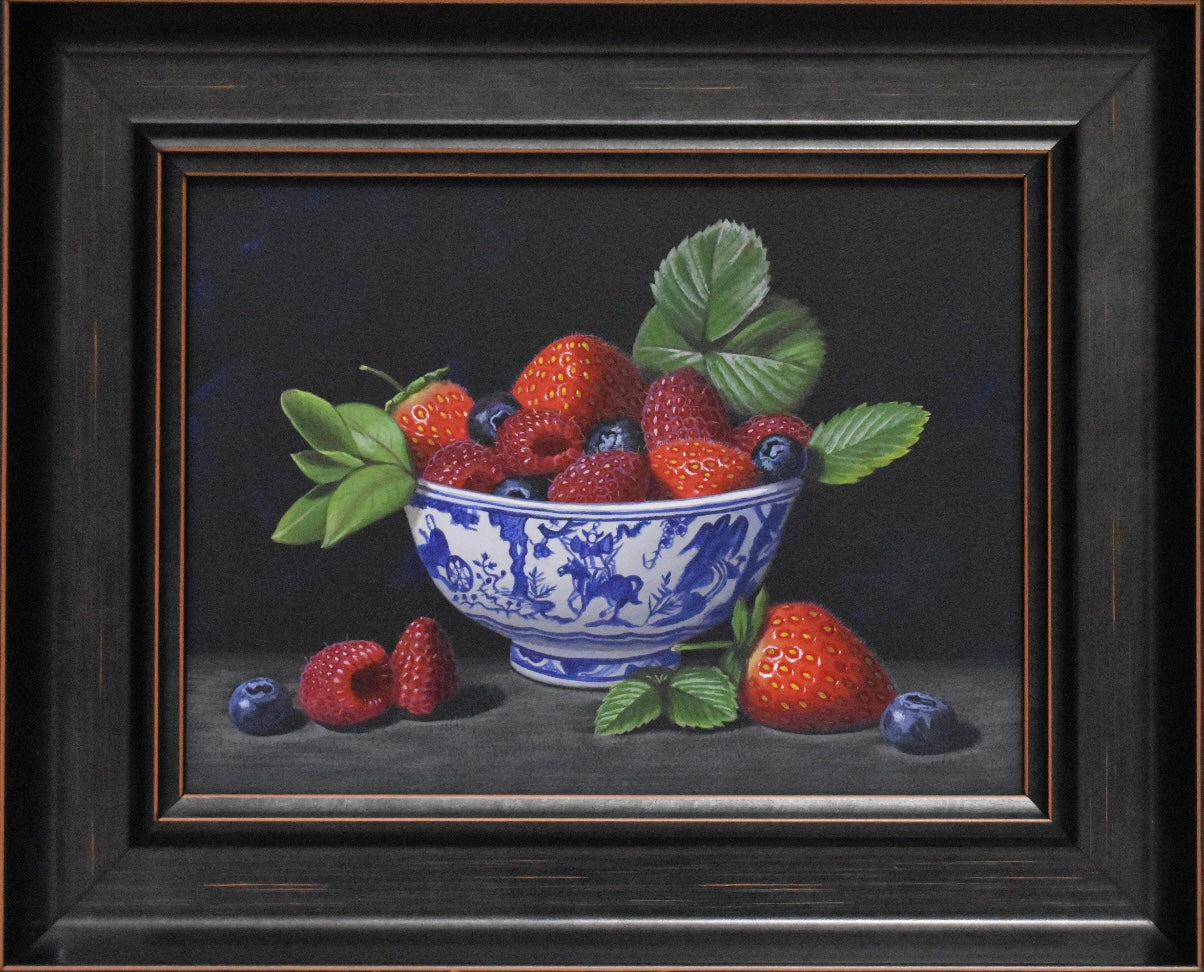 Framed still life painting of a blue and white bowl with strawberries and raspberries on a dark background.