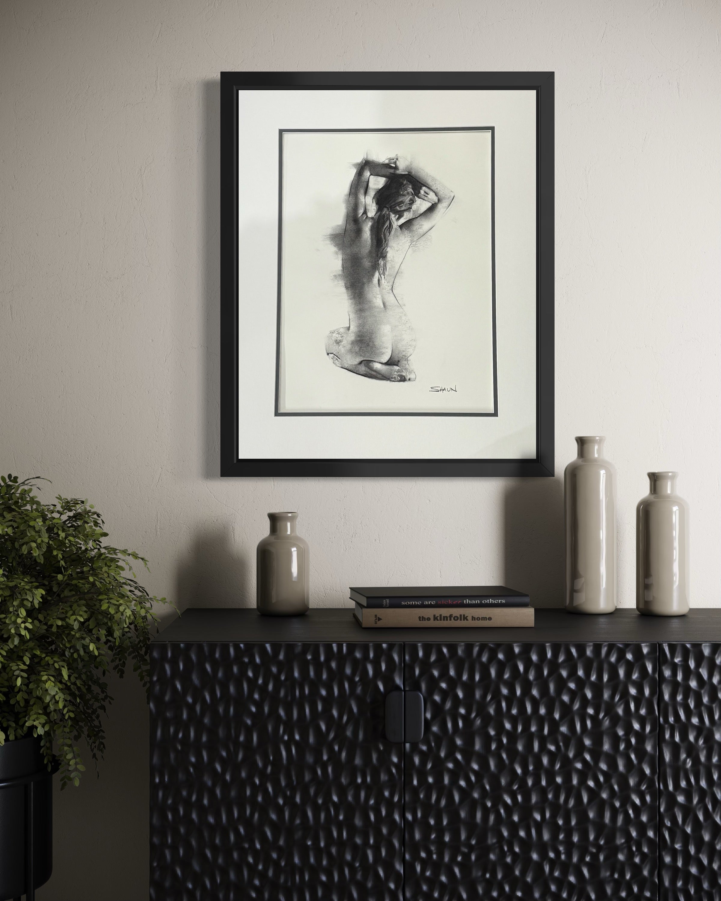 Framed artwork on a wall above a textured black cabinet with decorative bottles.