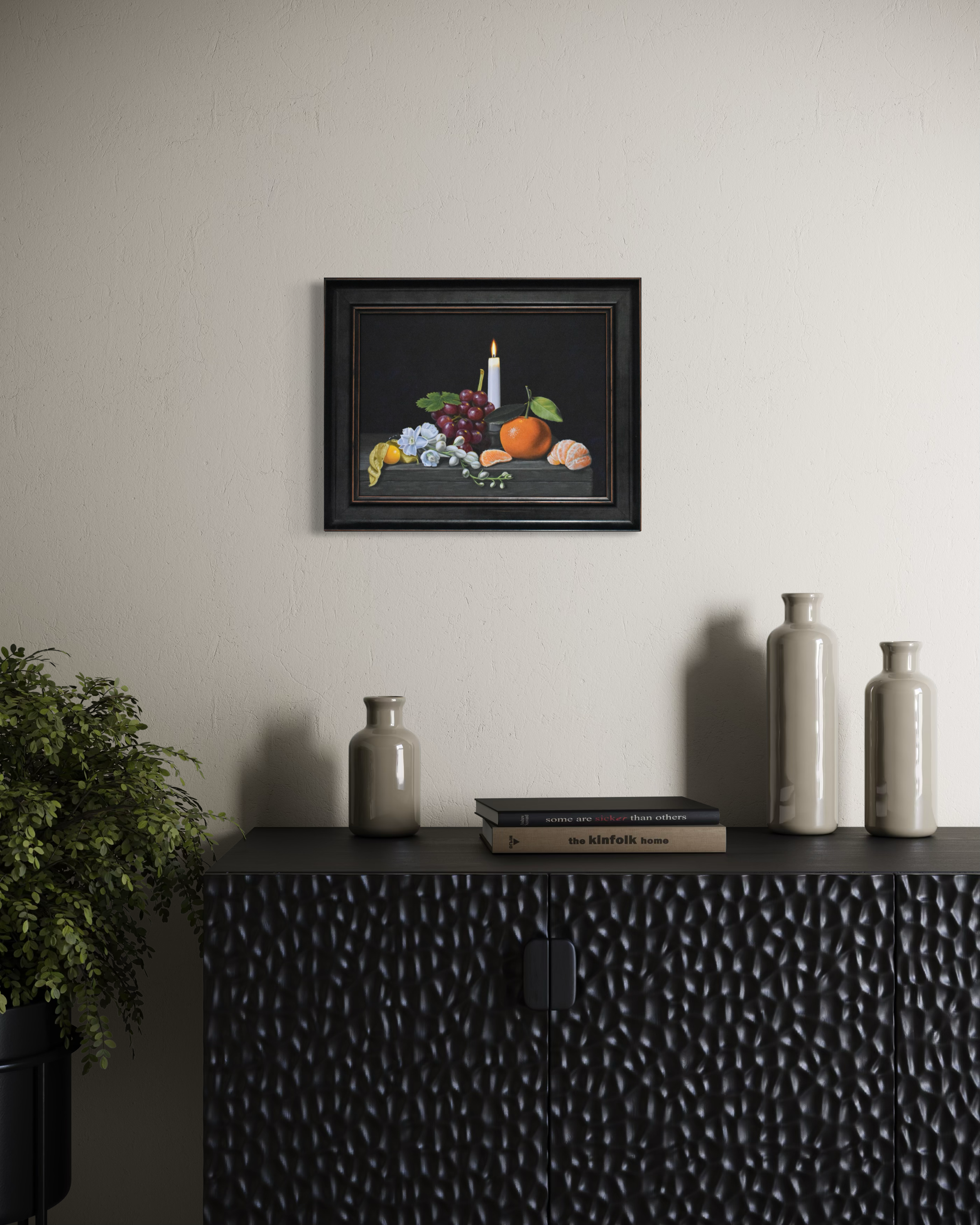 Framed still life painting on a wall above a black textured cabinet with decorative items.