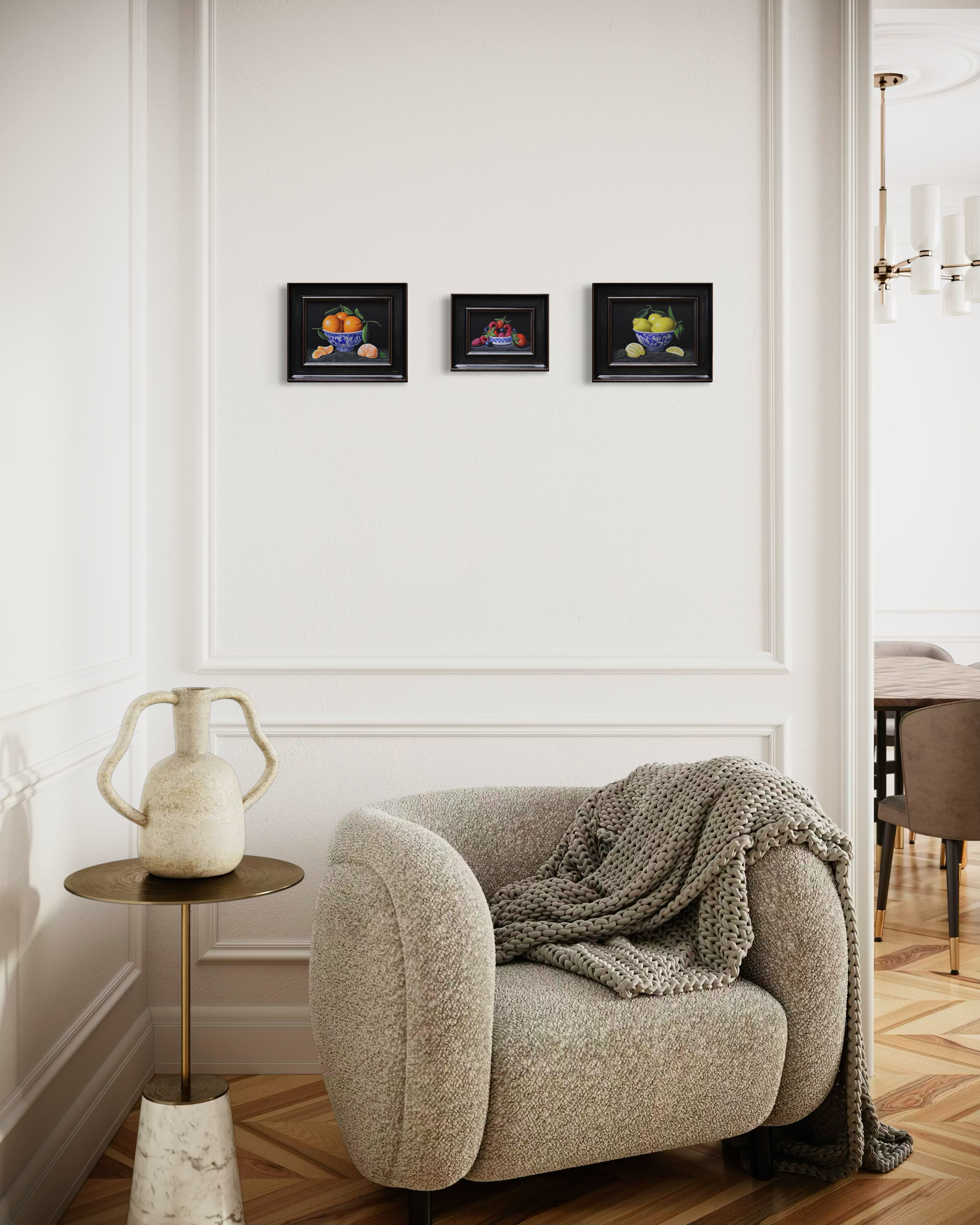 interior with a white wall with panelling and three still life paintings hanging horizontally above a speckled grey chair