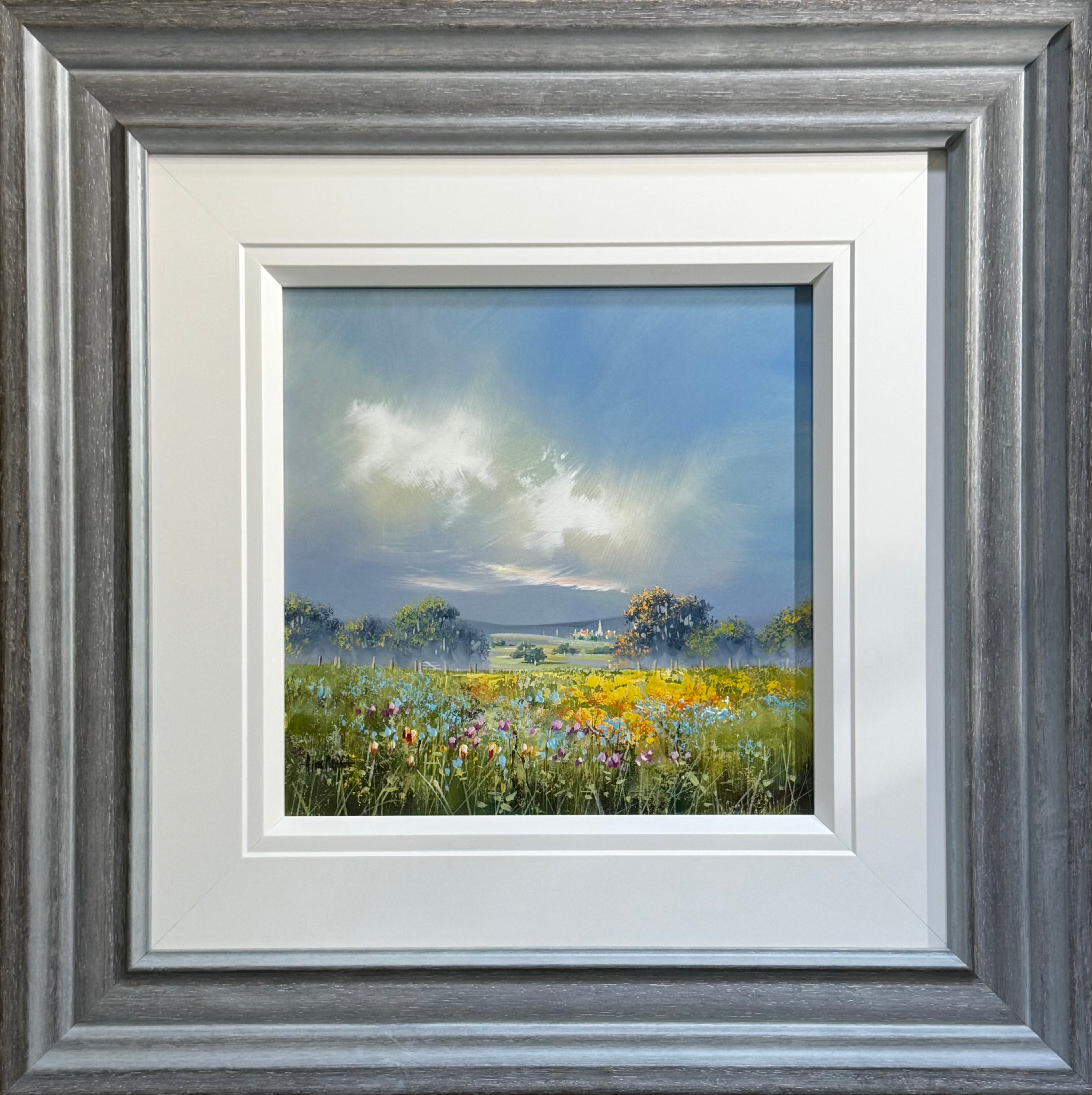Framed landscape painting of a wildflower meadow under a cloudy sky, presented in a wide gray wood frame with white matting.