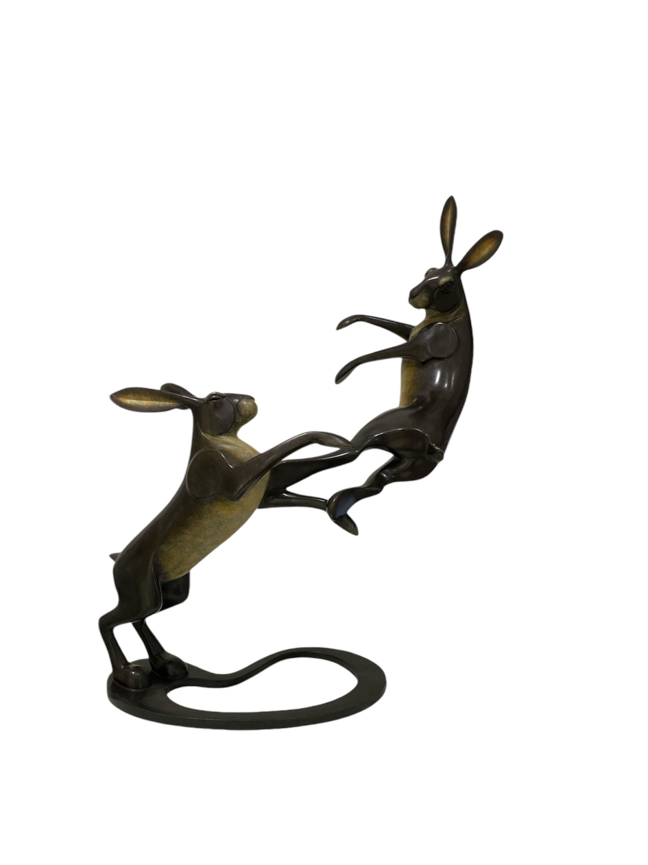 Bronze sculpture of two hares in a dynamic pose on a white background
