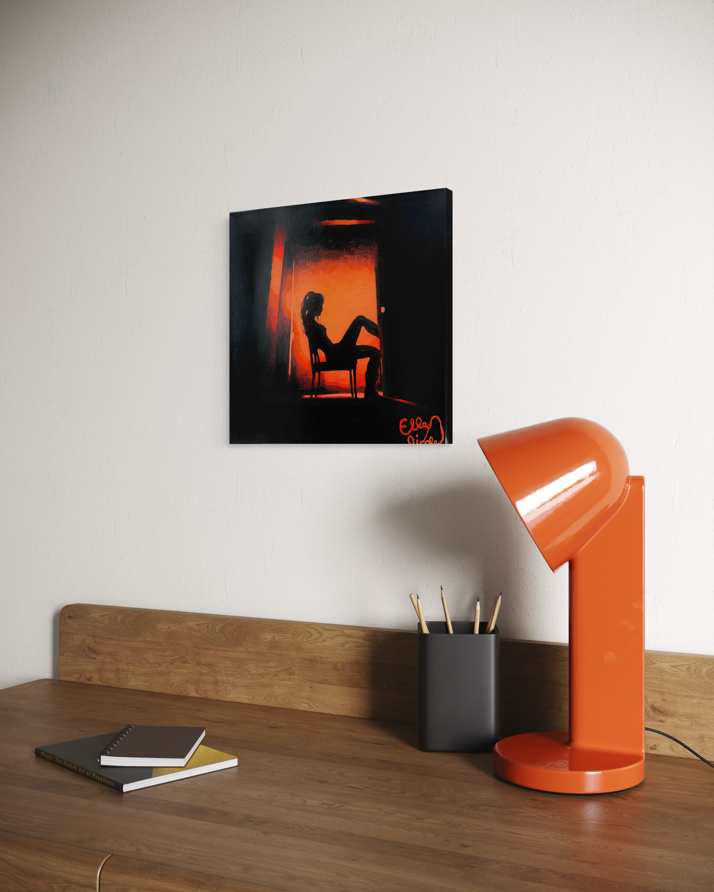Orange lamp on a wooden desk with a framed artwork of a silhouette in a red room.