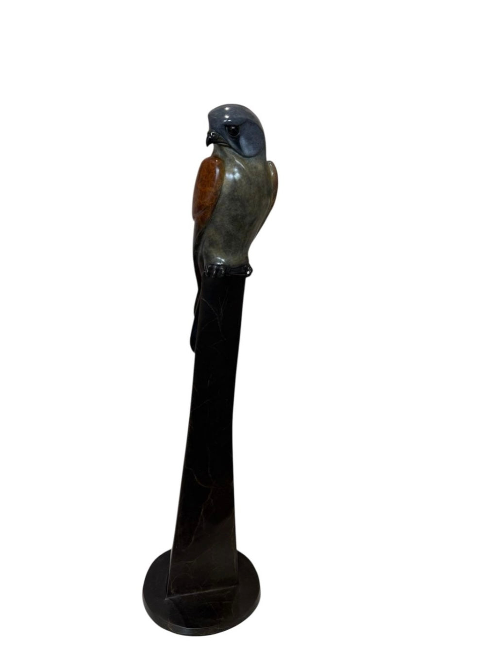 Statue of a kestrel perched on a black pedestal against a white background