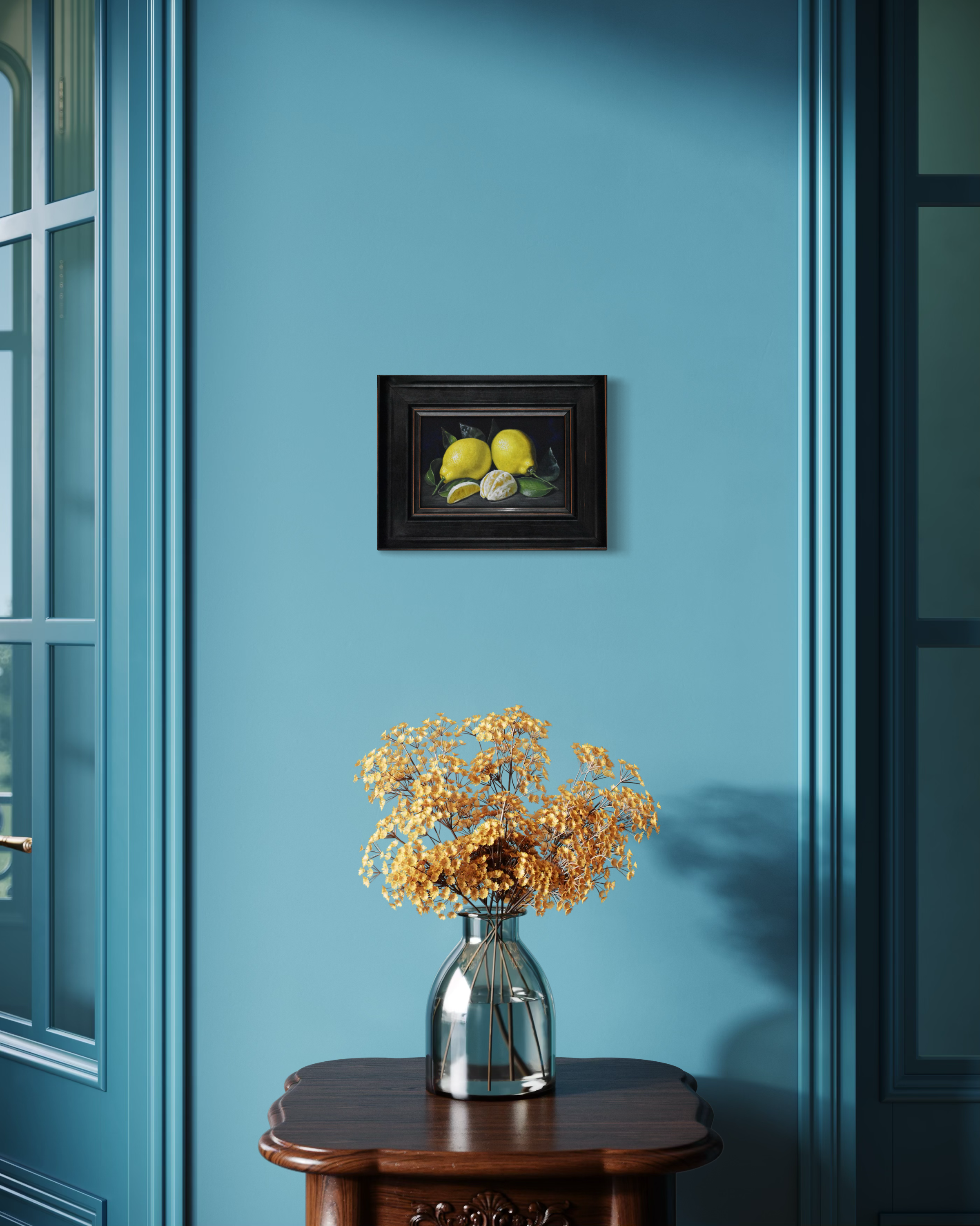Framed artwork of lemons on a blue wall above a vase with dried flowers.