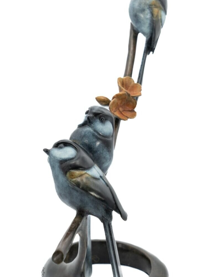 Statue of two birds perched on a branch with leaves against a white background