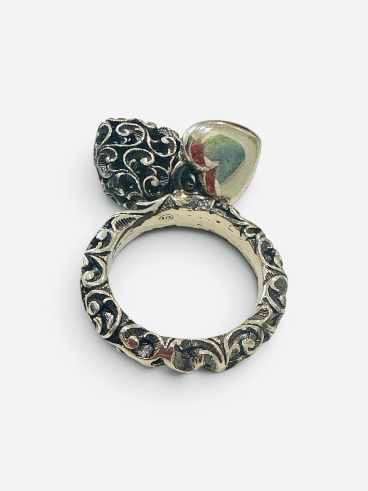 An ornate vintage ring featuring a textured silver filigree band, a black enamel floral accent, and a heart-shaped cabochon with a colorful landscape design, shown on a light gray background.