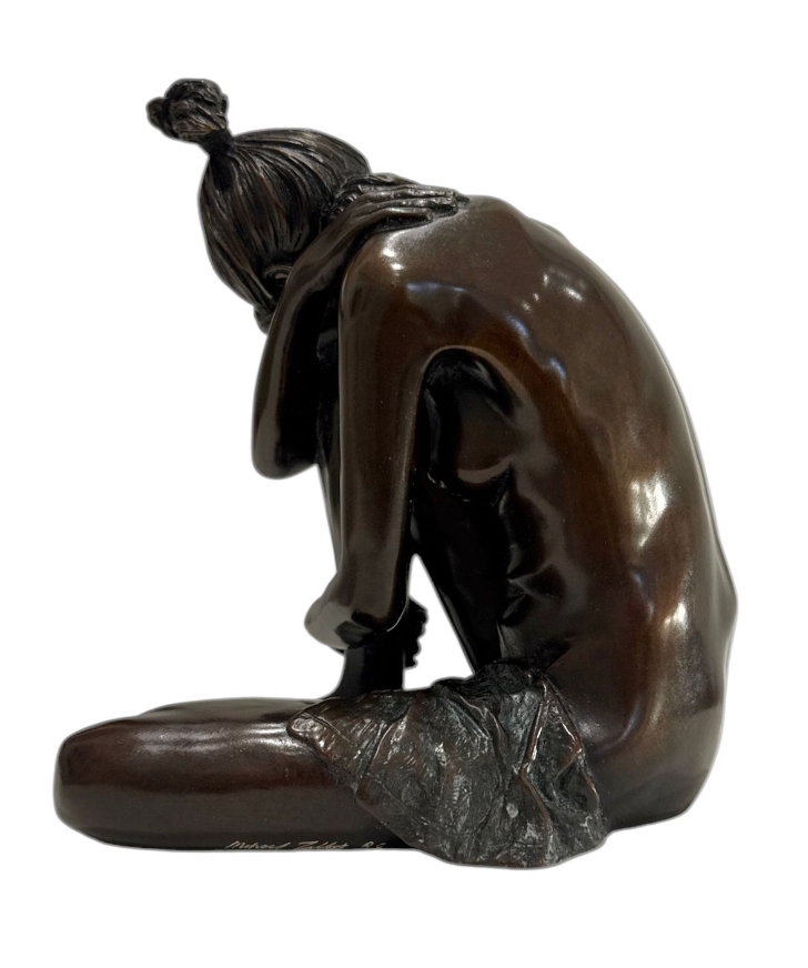 Bronze sculpture of a seated figure with a covered face on a white background