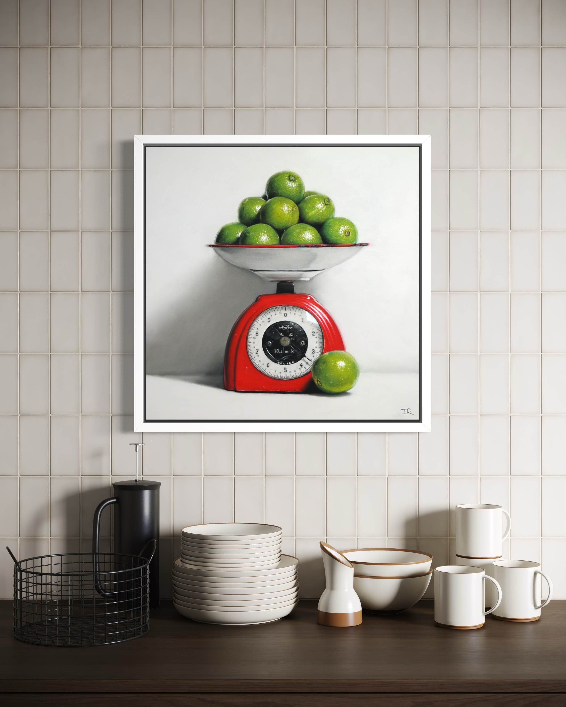 Framed artwork of a red kitchen scale with green apples on a tiled wall above a kitchen counter.