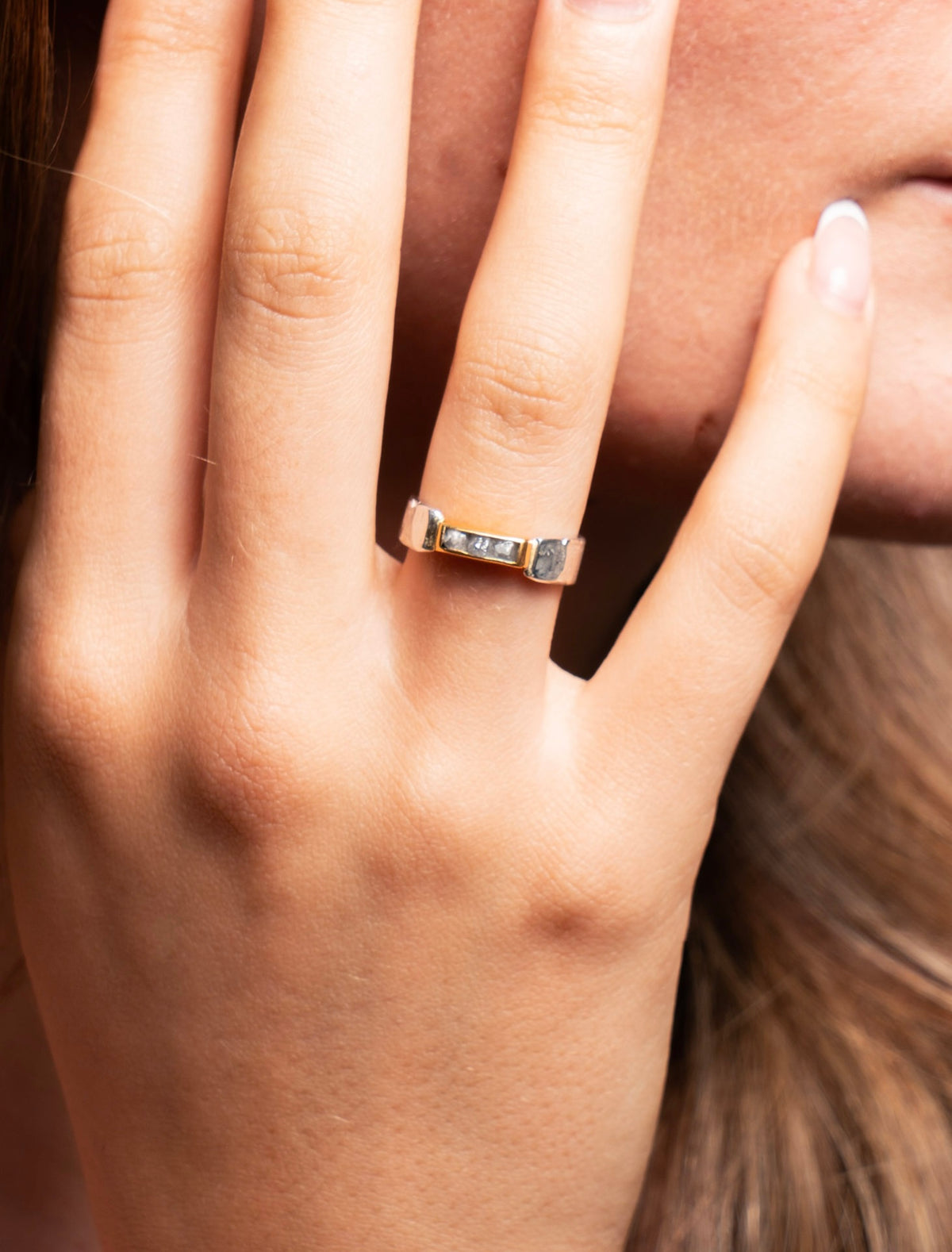 slim silver ring with rough diamonds in a gold setting on a tanned hand