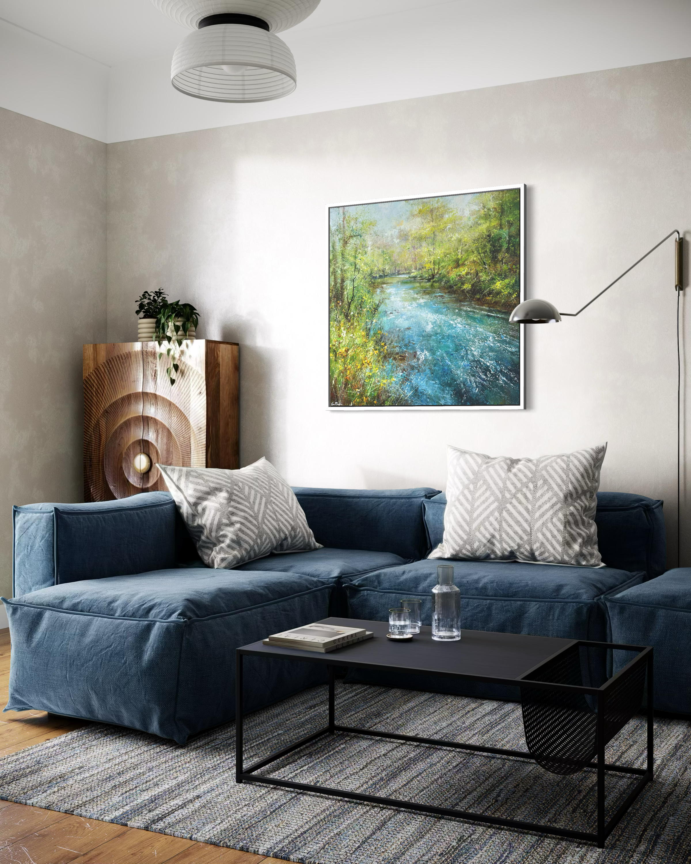 An original Derbyshire landscape painting of the River Dove by British artist Steve McLoughlin shown displayed in an interior settiing above. Blue sofa on cream walls