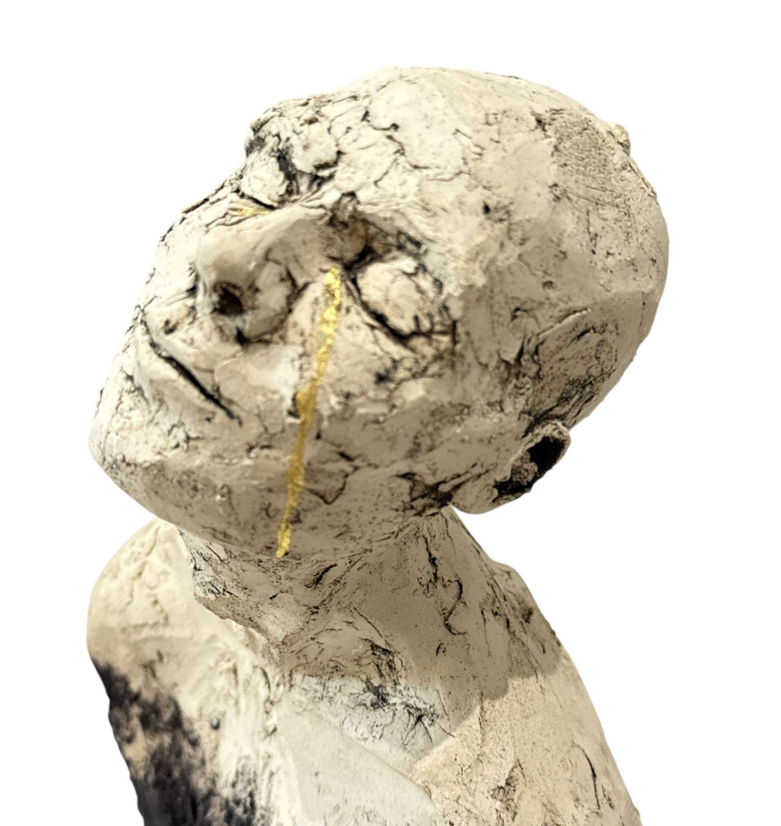 Clay sculpture of a figure with a gold necklace on a white background