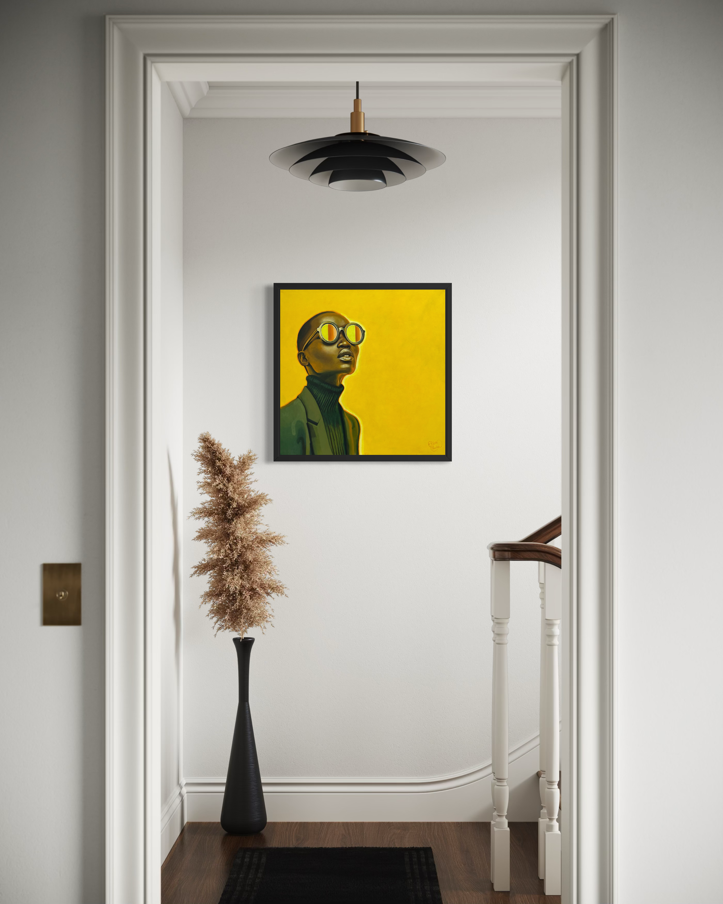 Yellow-framed portrait of a person with sunglasses on a wall in a room with a black vase and dried plant.