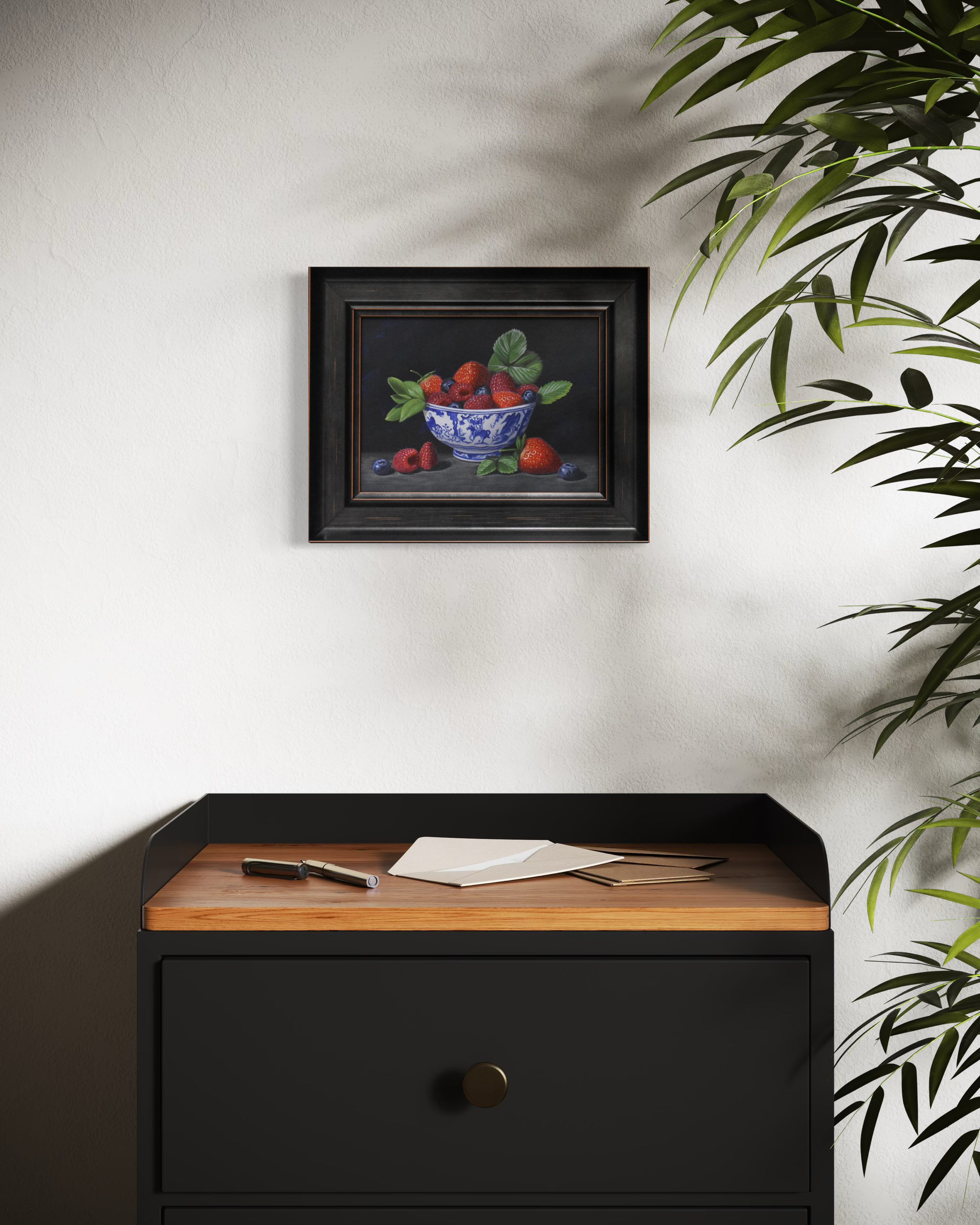 Framed still life painting on a wall above a black cabinet with wooden top.