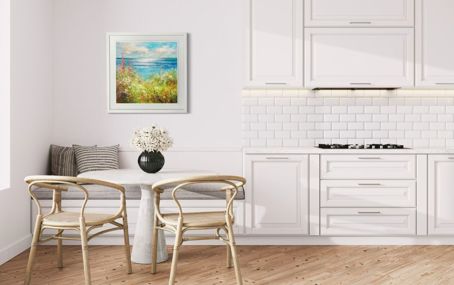 Modern kitchen with white cabinetry, wooden floor, and a small dining area with a colourful coastal painting hung on the wall