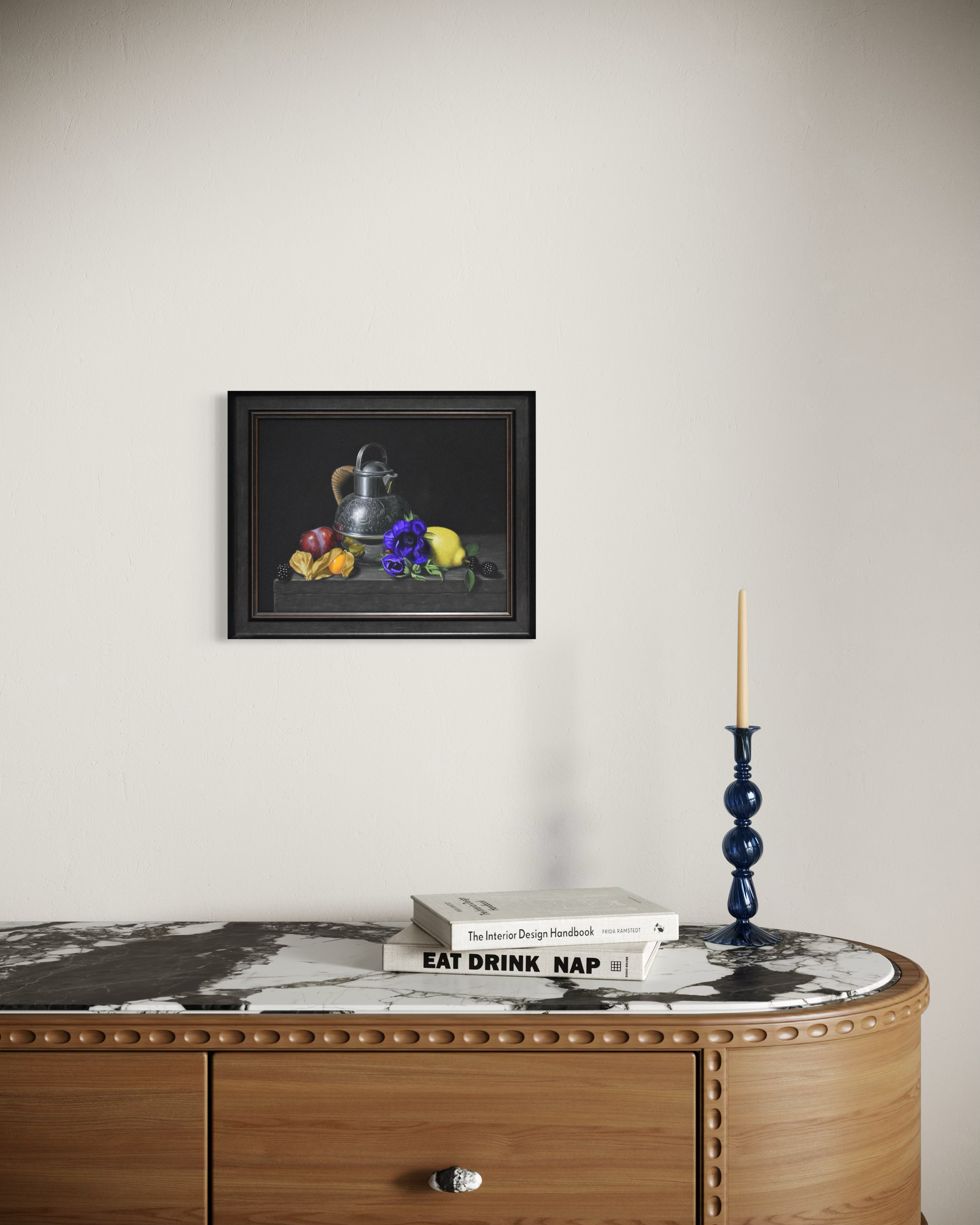 Framed still life painting above a wooden cabinet with decorative items.